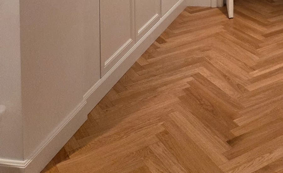 Battiscopa bianco posato lungo un mobile a muro, su pavimento in legno a spina di pesce