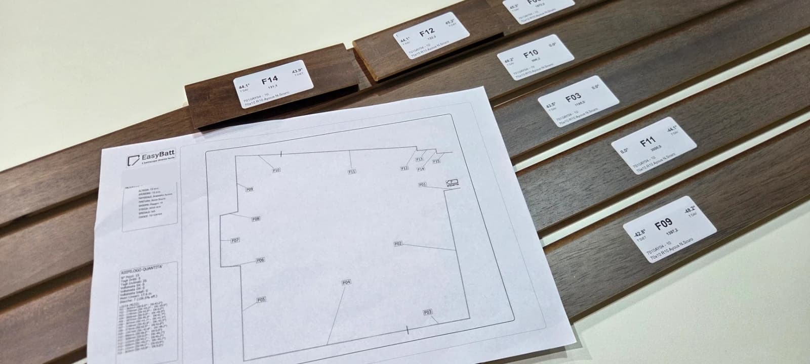 Battiscopa in legno già tagliati, ognuno con l'etichetta del suo codice, accanto alla planimetria di posa